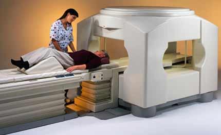 Photo of an open MRI unit. A technologist is shown attending a patient lying on the gantry.